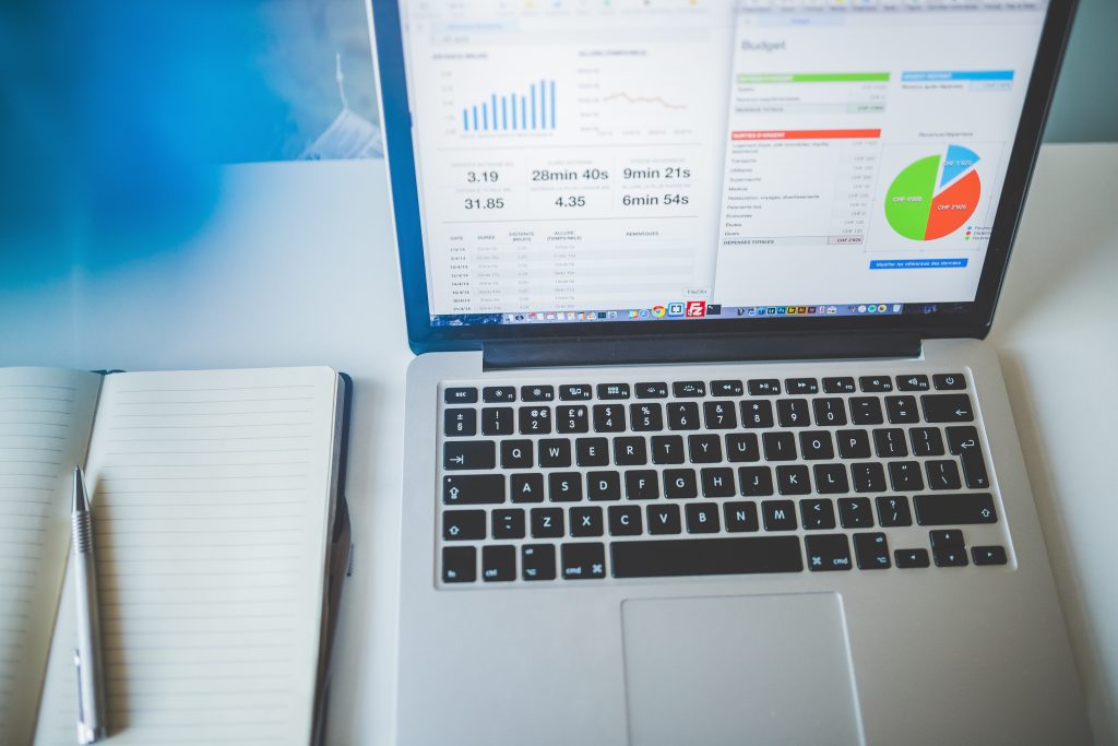 A laptop showing marketing stats with a pen and notepad next to it on the left hand side.